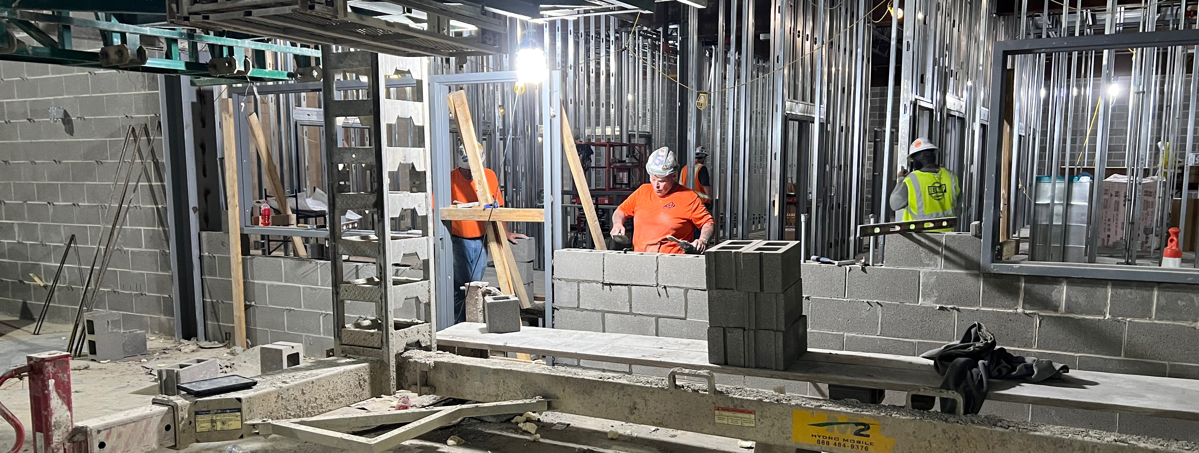 Three workers constructing a wall in an unfinished building.